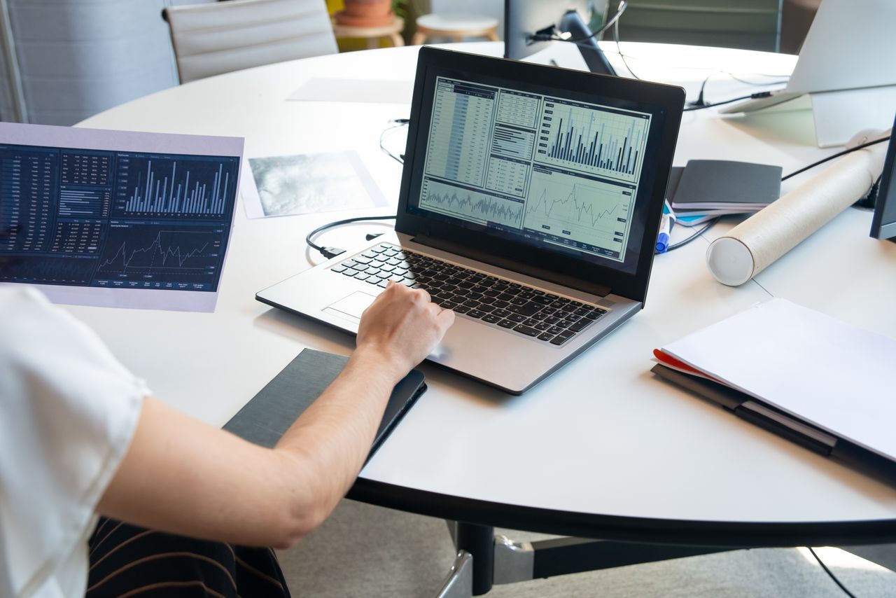 Business person evaluating financial charts on a laptop in a modern office setting.